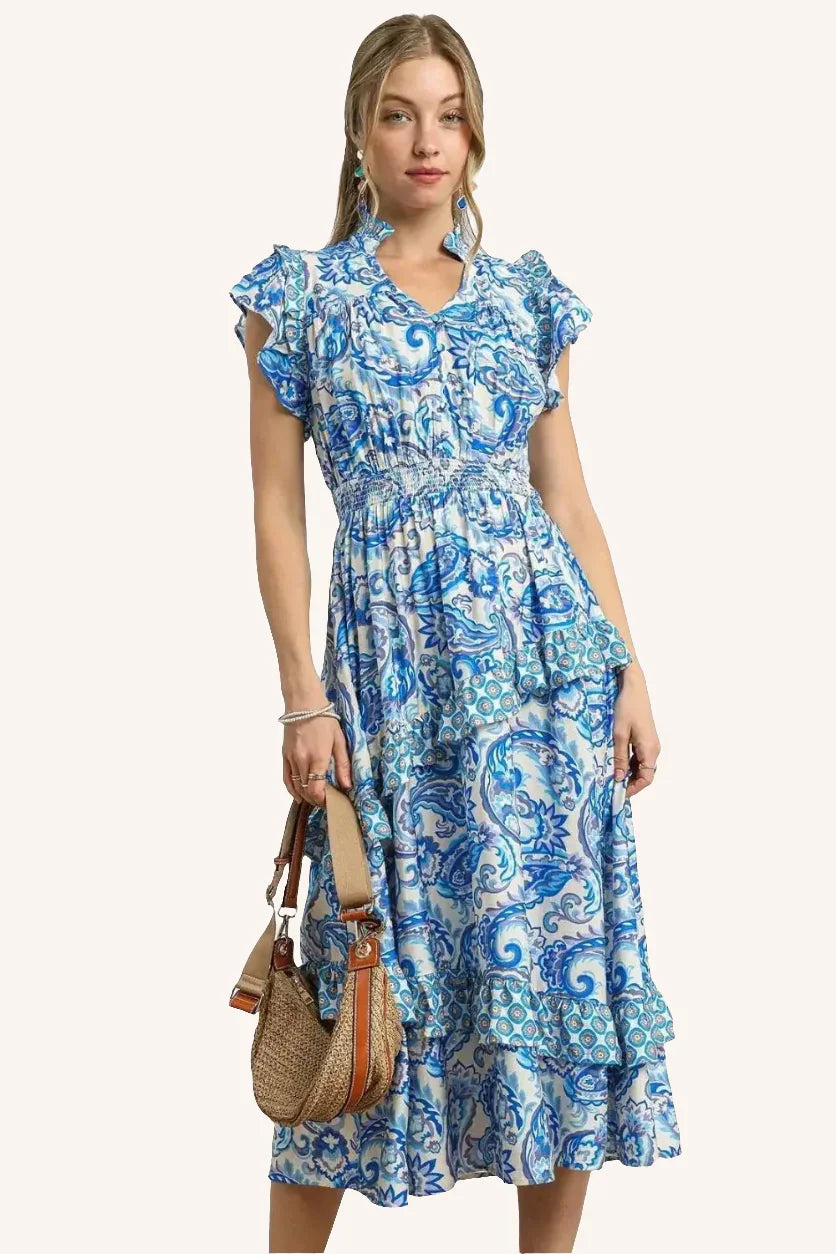 Woman in blue floral midi dress with ruffled sleeves holding a woven straw handbag